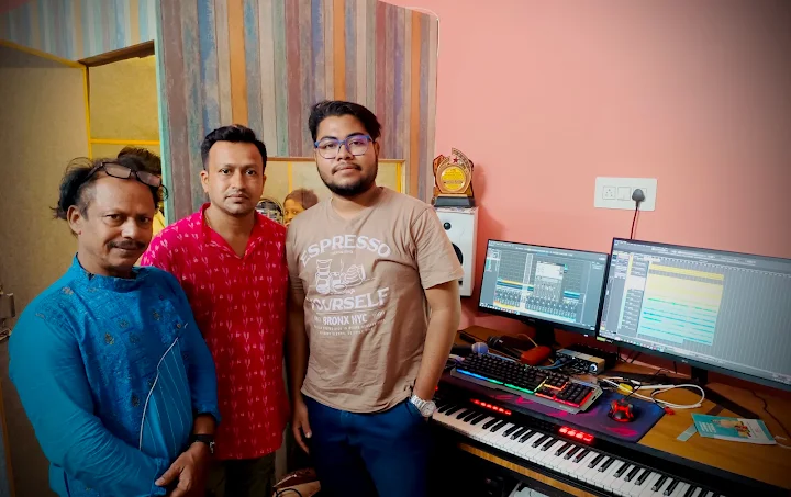 Three musicians at the T Music Lab production desk, with a recording session on two screens and a MIDI keyboard